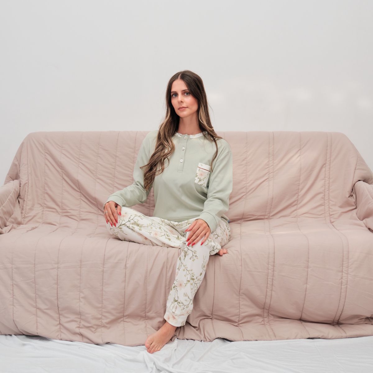 Mulher sentada num sofá a vestir pijama feminino quente verde em algodão cardado feito em Portugal, com botões no peito e calças de padrão floral.